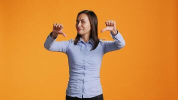 Asian person giving thumbs down in front of studio camera, expressing negativity and disapproval with dislike symbol. Negative woman showing rejection, being upset and displeased. video