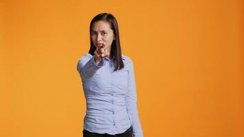 Asian model pointing at the camera in colorful studio, looking into the lens with confidence. Young filipino woman points index finger and standing proud against orange background. video