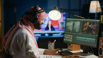 Muslim cinematographer wearing headphones while editing project, creating film montage, working with images and sounds. Man using video cutting software to process movie on PC workstation photo