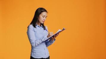 Filipino model writes information on files with clipboard, taking notes to create full report in front of camera. Young adult in casual clothing filling in documents, keeping track of something, video