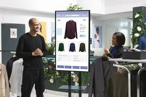 Male customer is shown clothing on an interactive kiosk board by female assistant in mall clothing store. Asian retail employee assisting a client who is selfordering modern fashion items. photo