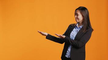 Businesswoman shows left and right directions in studio, creating new internet advertisement over orange background. Asian person working on marketing web commercial on camera. video