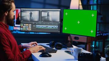 Video editor trimming segments of drone shot footage, using green screen PC monitor to work. Videographer splicing film pieces, editing them using professional software on mockup computer display photo