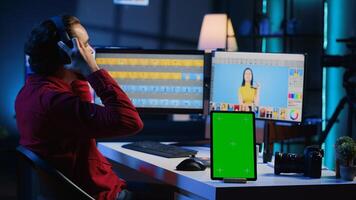 Chroma key tablet on desk next to photo editor working in independent production company. Isolated screen device and photographer adjusting white balance on overexposed pictures