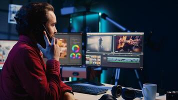 Video editor receiving phone call while arranging recorded stock clips into seamless whole in creative media studio. Videographer talking with director on smartphone while assembling recorded footage photo