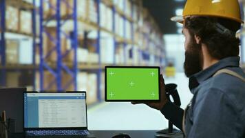 Packaging manager holding tablet with greenscreen in facility, working in storehouse with isolated copyspace template. Professional depot worker examines gadget with chromakey screen. photo