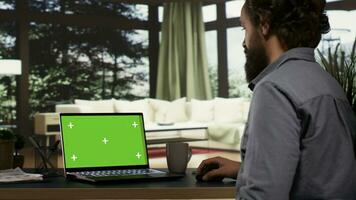 Young millionaire checks greenscreen template on laptop, getting cozy in his extravagant mountain resort. Wealthy businessman looks at blank mockup display on pc, teleworking. photo