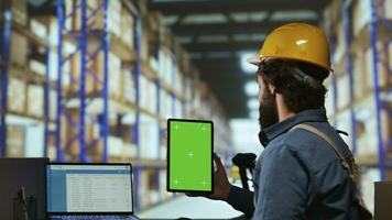 Warehouse operator holds greenscreen on tablet before working on merchandise distribution, examining isolated display on mobile device. Industrial staff member looks at blank chromakey screen. photo