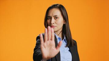 Filipino woman showing stop sign with palm, advertising negativity and no symbol on camera. Female model wearing formal attire in studio, showcasing rejection and refusing something. photo