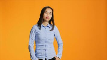 Portrait of carefree asian girl posing with confidence, wearing blue shirt and feeling confident in studio. Pretty filipino person standing over orange background, smiling with elegance. photo
