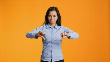 Asian woman giving dislike gesture on camera, showing disagreement and negativity over orange background. Negative unhappy adult presenting thumbs down symbol in studio, wrong idea. photo