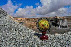 a globe on a stand in front of a rocky landscape photo