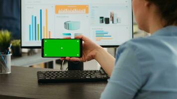 trabajador examina vacío Bosquejo diseño en de moda Teléfono móvil con pantalla verde mostrar. trabajando en teléfono inteligente y computadora a agencia oficina escritorio, analizando móvil software con blanco clave de croma foto