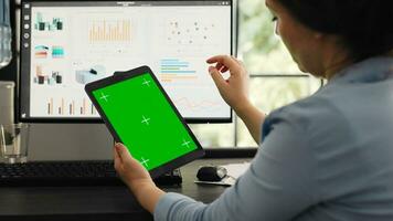 Specialist checking blank greenscreen template in coworking space, working on startup office tasks and looking at isolated copyspace display. Woman holding tablet with blank chromakey. photo