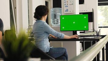 Office worker checks greenscreen monitor at desk, working on business operations with blank copyspace template on computer desktop. Person typing information and examining isolated mockup. photo