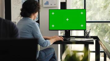 Businesswoman examining desktop with greenscreen at office desk in coworking space, using computer with chromakey and isolated display. Company employee reviewing blank copyspace monitor. photo