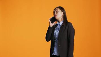 mujer de negocios utilizando teléfono inteligente a tomar remoto llamada en estudio, respondiendo móvil teléfono y hablando en frente de cámara. hembra modelo con chaqueta teniendo conversacion con jefe en dispositivo. video