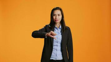 Asian employee showing dislike sign in front of camera, presenting thumbs down with unhappy facial expressions. Young adult does rejection and disagreement symbol over orange backdrop. video