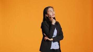 Thoughtful businesswoman posing over orange backdrop, thinking about new ideas and being in doubt. Clueless uncertain person brainstorming solutions, acting focused in front of camera. video