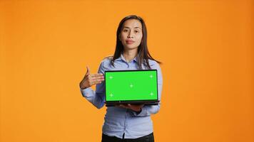 Confident adult showing laptop with greenscreen in studio, presenting isolated mockup template on wireless computer. Asian person holding pc with chromakey display on camera. photo