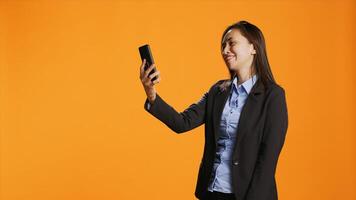 Filipino employee connecting online on videocall using smartphone, standing over orange background. Young woman with confidence answering videoconference connection on internet. photo