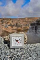 a small clock on rocks in the middle of a desert photo