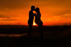 siluetas de marido y embarazada esposa besos mientras ellos disfrutar gasto hora juntos al aire libre imagen. foto