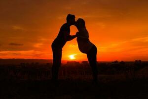 Silhouettes of husband and pregnant wife kissing while they enjoy spending time together outdoor.Toned image. photo