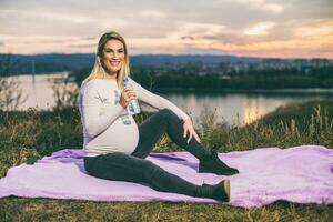 Beautiful pregnant woman enjoys drinking water while spending time outdoor. photo