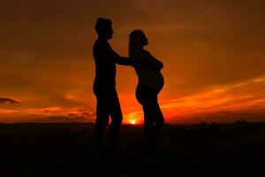 Silhouettes of husband and angry pregnant wife while they standing outdoor.Toned image. photo