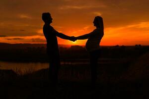 Silhouettes of husband and pregnant wife holding hand and enjoy spending time together outdoor.Toned image. photo