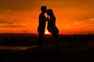 Silhouettes of husband kissing his pregnant wife into forehead and enjoy spending time together outdoor.Toned image. photo