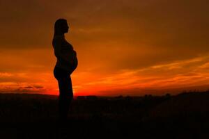 Silhouette of pregnant woman enjoys spending time outdoor.Toned image. photo