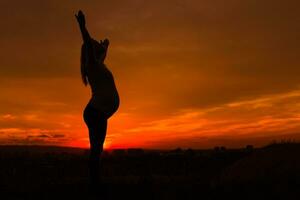 Silhouette of pregnant woman with arms outstretched enjoys spending time outdoor.Toned image. photo