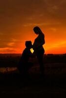 Silhouettes of husband kissing stomach of his pregnant wife while they enjoy spending time together outdoor.Toned image. photo