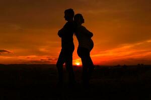 Silhouettes of husband and pregnant wife having conflict while they standing outdoor.Toned image. photo