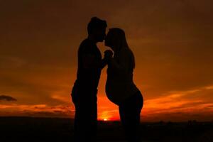 Silhouettes of husband kissing his pregnant wife into nose and enjoy spending time together outdoor.Toned image. photo
