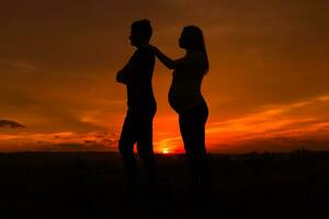 Silhouettes of angry husband and  pregnant wife while they standing outdoor.Toned image. photo