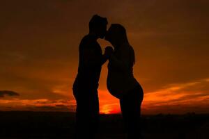 Silhouettes of husband and pregnant wife kissing while they enjoy spending time together outdoor.Toned image. photo