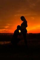 Silhouettes of husband listening belly of his pregnant wife while they enjoy spending time together outdoor.Toned image. photo