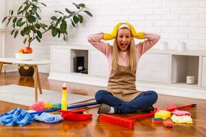 Image of  overworked housewife with cleaning equipment shouting while sitting in the living room. photo