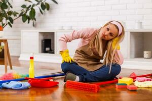 Tired housewife with cleaning equipment sitting in the living room. photo