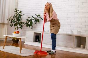 Tired housewife cleaning living room with a broom. photo