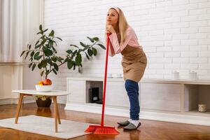Tired housewife cleaning living room with a broom. photo