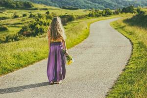 mujer en un púrpura vestir caminando abajo un la carretera y participación flores foto