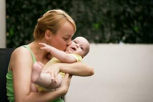 madre disfruta participación y besos su pequeño alegre bebé chico. foto