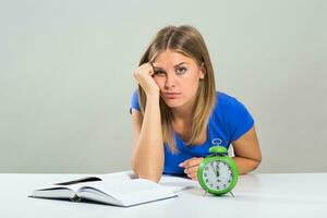 Sad female student doesn't want to study,but the clock is showing that there is not to much time. photo