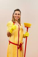 Portrait of beautiful housewife holding broom and showing thumb up photo