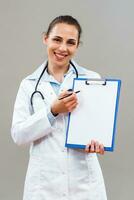 Beautiful female doctor is holding clipboard and showing document with pen. photo