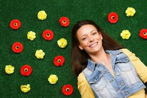 Beautiful young woman enjoys lying on the grass with a lot of flowers around her photo